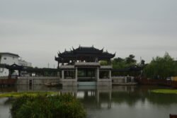 a lagoon with an ornate chinese-style water gate as entrance to a town, with a building behind it.