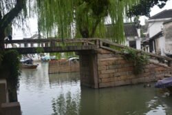 a stone bridge with flat walkway crossing over a canal, with a tree on the left side