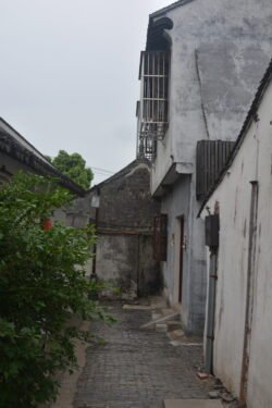 a straight walkway of pavestones winding through an alley with small buildings on each side.