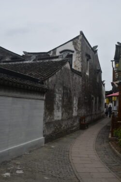 a curved walkway of pavestones winding through an alley with small buildings on each side.