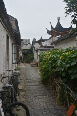 alleyway with a group of bicycles parked along the left house wall, ornate chinese-style roofs top the buildings