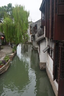 narrow canal with a small plaza with tree on the left, houses built right up to the right edge.