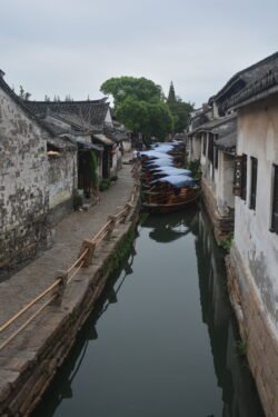 narrow canal with walkways on each side, and a group of sampan canal boats moored across the width of the canal.