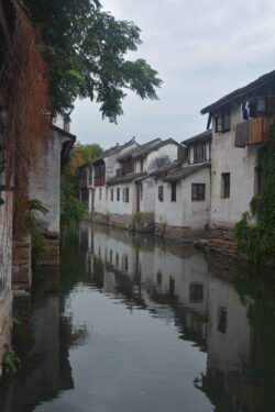 wide canal lined with stone buildings on each side. The images of the buildings are reflected in the calm water of the canal