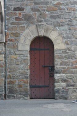 heavy masonry wall with arched doorway. The door is made of heavy wood planks with exposed iron studs and large iron hinges.