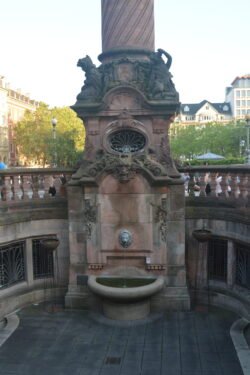an ornate stone fountain supporting a stone column, and stone railing behind it