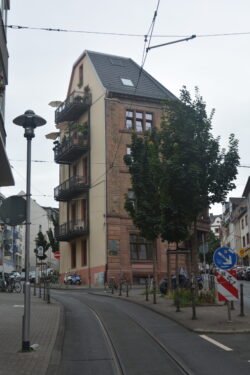narrow stucco and brick residential building. A city street with trolly track curves uphill towards the building