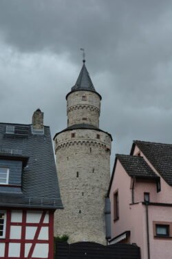a cylindrical white stone tower with conical roof tucked behind two buildings.