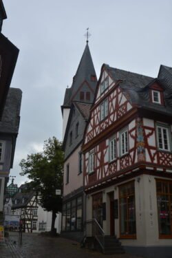 a highly decorative half-timbered house with a prominent church steeple behind it