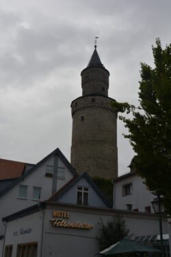 a cylindrical white stone tower with conical roof tucked behind a building with sign indicating it is a hotel.