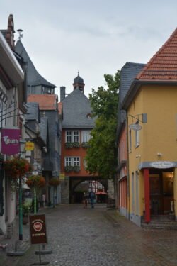 a cobblestone street leading to an archway across the road, with half-timbered houses on each side.