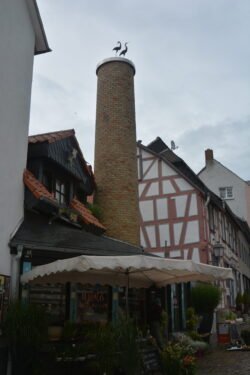a cylindrical brick chimney with metal bird sculptures on top. The chimney is poking out of a restaurant with the wall of a half-timbered house next to it.