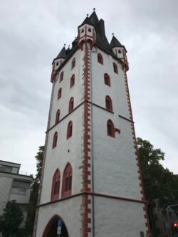 looking up at a white square tower with red brick corners and red-framed arched windows