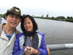 a man and a woman taking a selfie with a wide canal behind them. In the distance are dutch windmills.