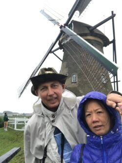 ron and weifang charest, dressed for rainy weather, with a dutch windmill behind them