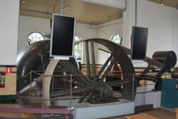 large pully wheel with belt and other machinery in a whitewashed room