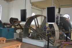 large pully wheel with belt and other machinery in a whitewashed room