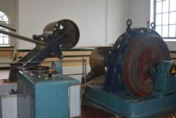 large pully wheel with belt and other machinery in a whitewashed room