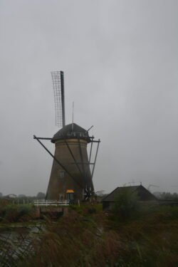 a view of a lone dutch windmill with small house next to it.