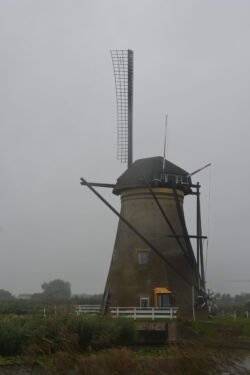 a dutch windmill with a stone lower body and four large sails on a rotating upper section