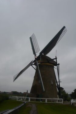 a view of a lone dutch windmill with white fence around it