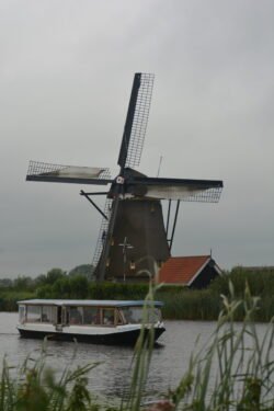 canal boat passing in front of a dutch windmill with red-roofed hut next to the windmill
