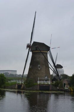 a large dutch windmill on edge of a caal, with another windmill in the distance behind it.