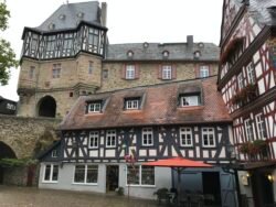 a courtyard with decorative half-timbered houses and a large stone castle behind and above them