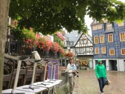 a man and a woman standing in a cobblestone road with a half-timbered house behind them.